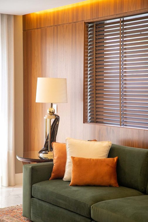 Sala com painel de madeira, sofá verde e luminária